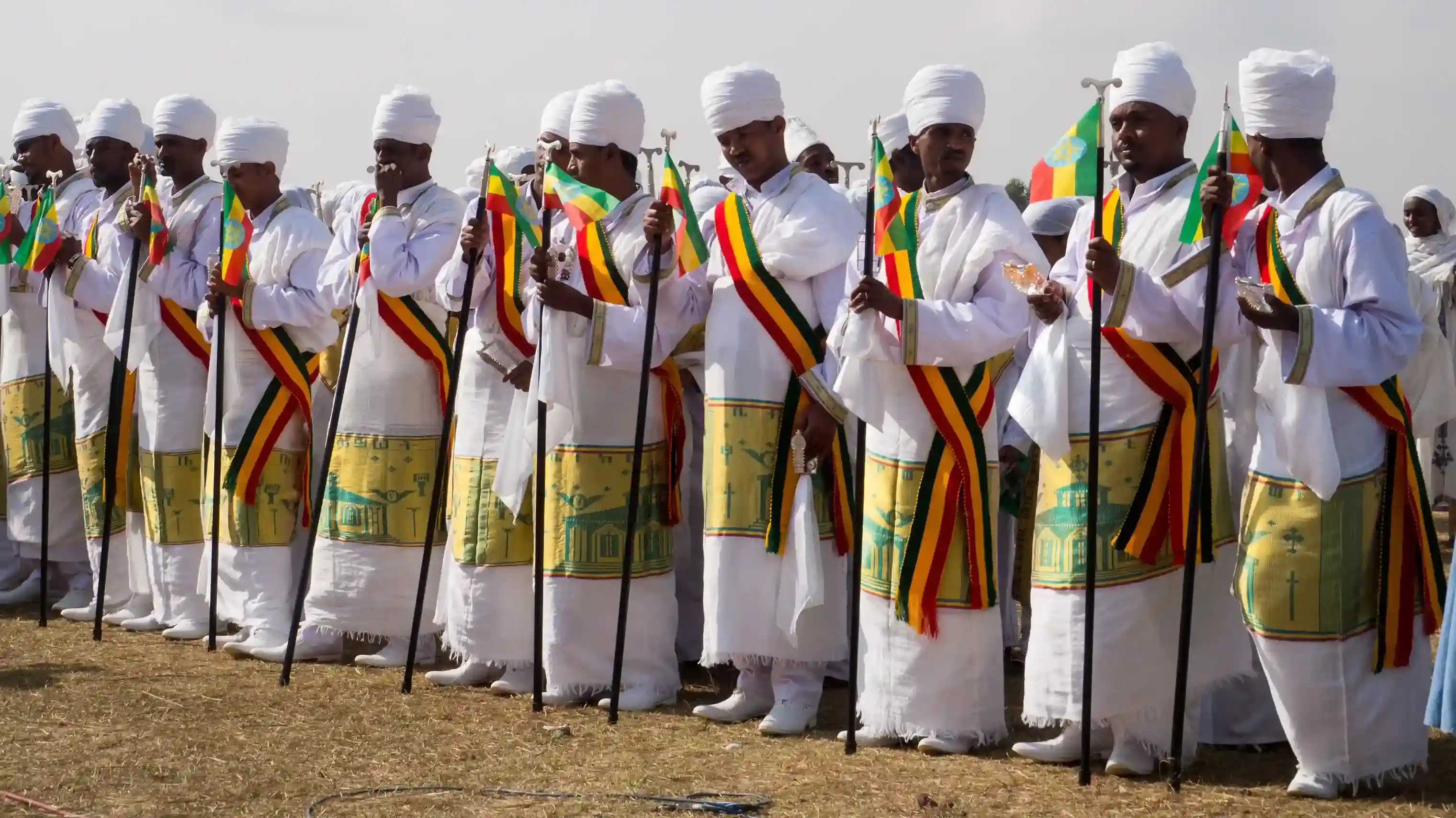Rows of Ethiopian Orthodox deacons carrying ceremonial staffs and flags during the Timkat procession